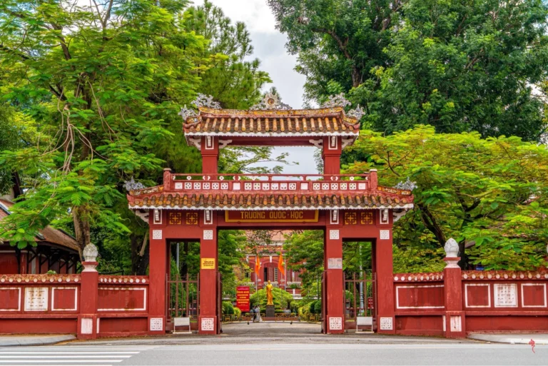 Ảnh trường Quốc Học Huế nhìn từ xa với sắc đỏ gạch đặc trưng bên dòng sông Hương
